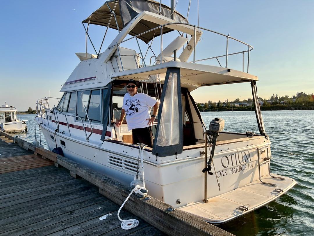 OTIUM, a white Bayliner flybridge cruiser, tied stern-to at a wooden dock in evening light. The transom is lettered OTIUM, OAK HARBOR WA.